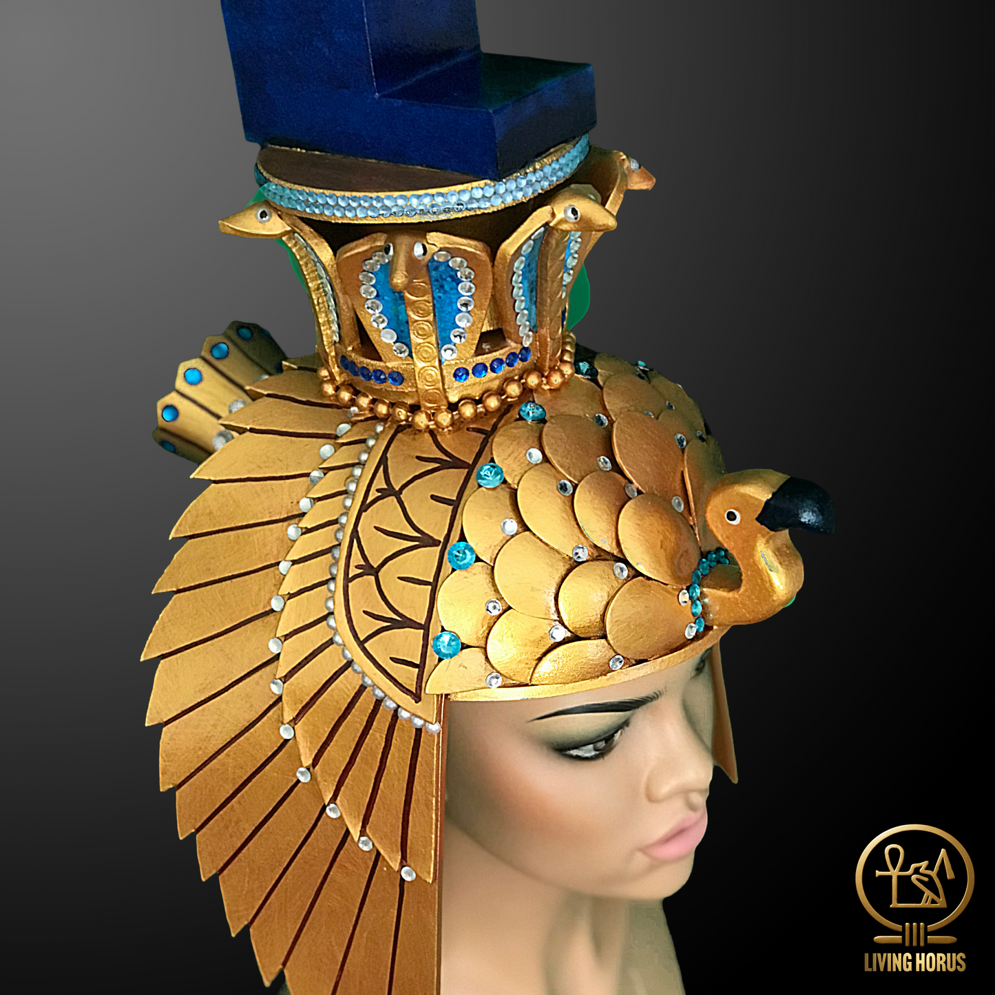 Decorative headdress with gold feathers and blue accents on a mannequin head, brand 'Living Horus' visible.